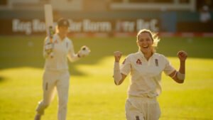 England cricketer Alice Capsey celebrating her unbeaten innings with teammate Sophia Dunkley in background on sunlit cricket ground in Bengaluru