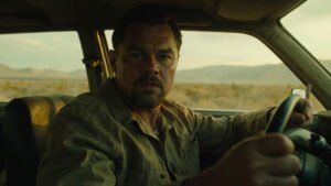 Leonardo DiCaprio as determined father Bob driving a car with tense expression, gritty American landscape blurring past window