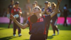 England cricketer Alice Capsey celebrating her unbeaten 88 runs on the cricket pitch in Bengaluru with teammates cheering in background