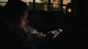 Person scrolling through tablet showing TV watchlist while relaxing on sofa in cozy living room at dusk