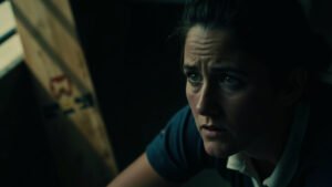 England women's cricketer in pensive moment inside dim pavilion with bat resting beside her, natural light casting soft shadows